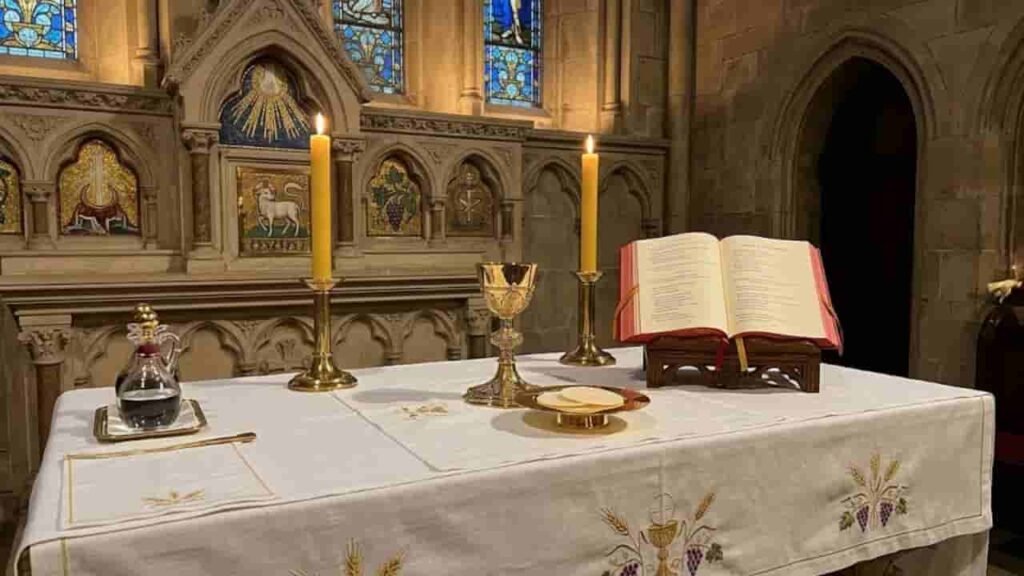 An open Roman Missal displays the Liturgy of the Eucharist on an altar prepared with a golden chalice, paten with hosts, communion cruets, and lit candles.