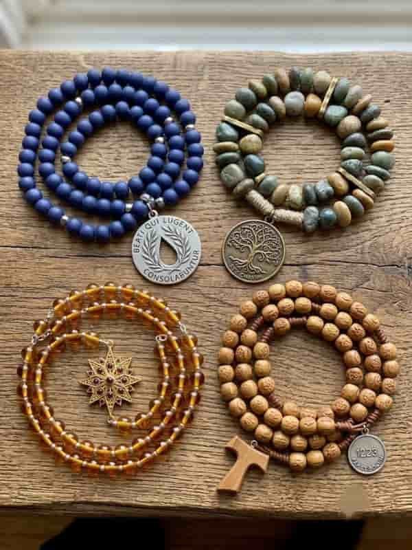 Collection of different types of Christian prayer beads and chaplets arranged neatly on a wooden surface.

Option 2: Detailed & Descriptive